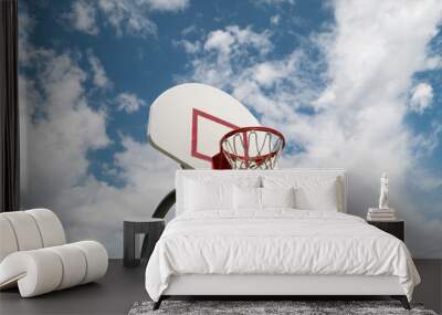 Blue, partly cloudy skies behind a lone basketball hoop. Wall mural