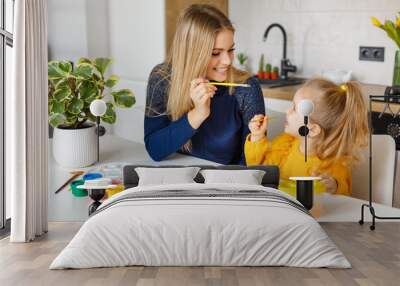 Mother and daughter painting at home. Cute little kid in yellow sweater having fun with parent and paints. Concept of early childhood education, hobby, talent, preschool leisure and parenting Wall mural