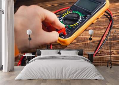 Multimeter and two test leads on a wooden background. A man's hand holds two test leads. A studio photo with hard lighting. Wall mural