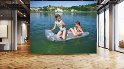 Two little cute girls in swimsuits swim on an inflatable mattress on a blue career lake. Wall mural