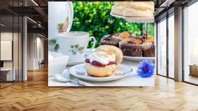 Afternoon tea with cakes and traditional English scones with strawberry jam and clotted cream set up on a table in the garden. Outdoor dining. Wall mural