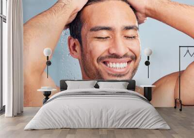 Smiling muscular asian man showering alone in a studio and washing his hair against a blue background. Fit and strong mixed race man standing under pouring water. Hispanic athlete enjoying hot shower Wall mural