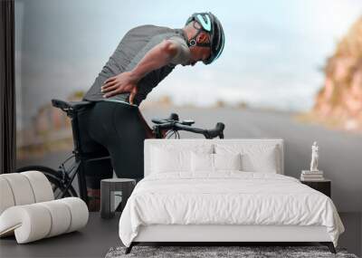 Fitness, sports injury and back pain by man cyclist feel uncomfortable while cycling along mountain route. Training, pain and injured athletic guy suffering from joint, muscle and spinal discomfort Wall mural