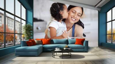 Happy latin mother and daughter baking and sharing a kiss while bonding. A young woman helping her daughter bake or cook while stirring the batter and giving an affectionate hug in the kitchen Wall mural