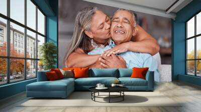 Happy senior couple hug in home, retirement lifestyle together in Mexico and relax on sofa. Romantic marriage life, love bonding time and elderly woman kissing latino husband on cheek in living room Wall mural