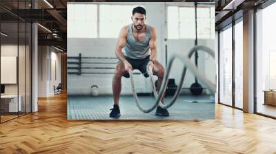 Never give up never surrender. Shot of a young man using the ropes in the gym to build arm strength. Wall mural