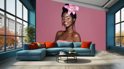 Pink lily hair style. Young Beautiful African American model with bunned hair smiling and posing against pink background Wall mural