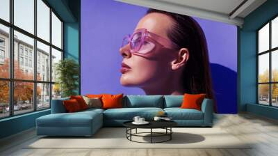 Profile portrait of a beautiful model in trendy square pink sunglasses with glossy make up posing against violet background.  Stylish glasses. Glance glamour picture. Summer Eye wear fashion . Wall mural