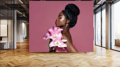 Profile portrait of young beautiful African American model posing with lily flowers against pink background Wall mural