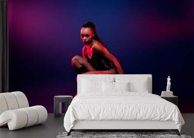 Photo of african american girl sitting posing wearing leather tight bodysuit boots isolated neon color background Wall mural