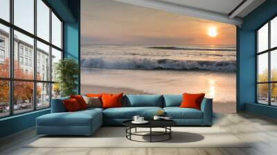 The sun rising over the ocean at sunrise with waves crashing ashore. Wall mural