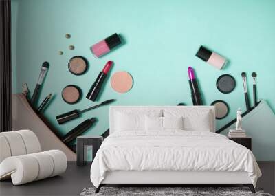 Make up products spilling out of a pastel colored cosmetics bags on to a turquoise background, with empty space above Wall mural