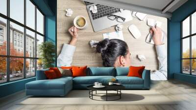 Top view of tired, overwoked businesswoman, office worker, lying on the desk with laptop, coffee and papers. Wall mural