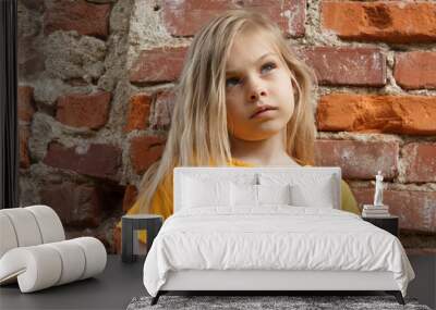 Beautiful little five-year-old girl with blond hair in yellow clothes on the background of an old brick wall. Wall mural