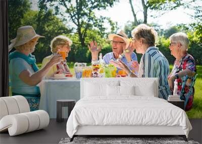 Senior friends having picnick with coffee and cake outdoors in sunshine. Wall mural