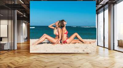 Two attractive young women sitting on the tropical beach at summer time. Bali island. Wall mural