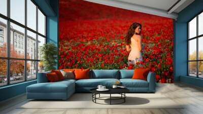 Beautiful and sexy long haired brunette woman stands in white dress in the middle of red flowery field. Wall mural