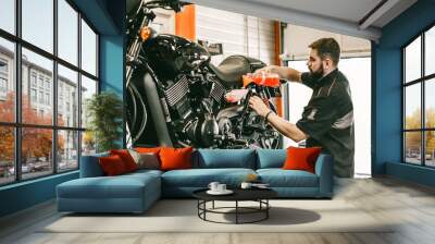 Professional mechanic pouring antifreeze into a motorcycle. Confident young man repairing motorcycle in repair shop. Wall mural