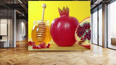 A vibrant red pomegranate and honey jar against a bright yellow background. Wall mural