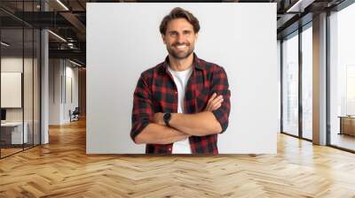 Confident young man in casual attire smiling with arms crossed against a plain background. Wall mural