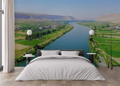 Serene landscape of a river winding through lush green fields and hills. Wall mural