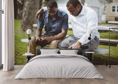 African-American male friends sitting on the bench praying with the Bible in their hands Wall mural