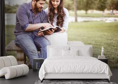 Closeup shot of a couple sitting on a bench and reading the bible with a blurred background Wall mural