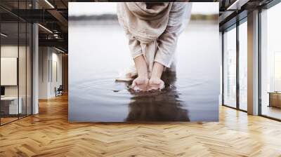 Closeup shot of a female wearing a biblical robe standing in the water while washing her hands Wall mural