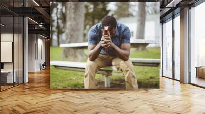 Closeup shot of a male sitting in a a park while holding the bible against his head Wall mural