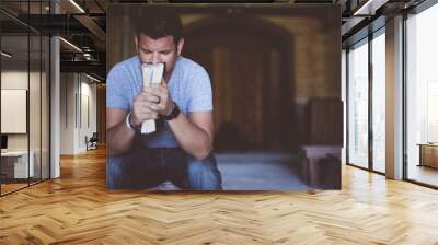 Closeup shot of male holding the bible in front of his mouth while praying with blurred background Wall mural