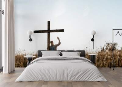 Male standing near a handmade wooden cross praying with his hand up Wall mural