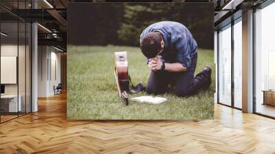 Man sitting on the grass and praying with a book and a guitar near him Wall mural