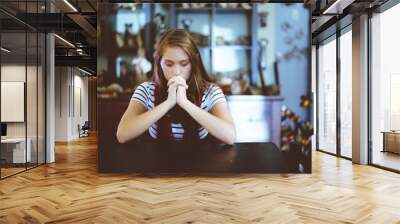 Shallow focus shot of a female sitting with her hands near her mouth while praying Wall mural