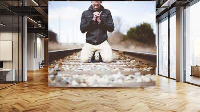 Shallow focus shot of a male on his knees on train tracks while praying Wall mural