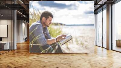 Shallow focus shot of a male sitting on the beach shore while reading the bible Wall mural