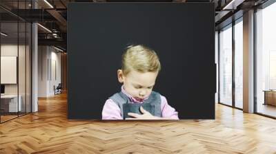 Vertical shot of a child holding the bible against his chest wit ha black background Wall mural