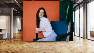 Attractive young woman poses for the camera sitting on the blue armchair Wall mural