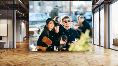 Couple in love with their pets sitting outdoor in city near caffe in spring. Funny unusual odd strange people spending time together. Family with domestic birds have fun. Fashionable pair lifestyle. Wall mural