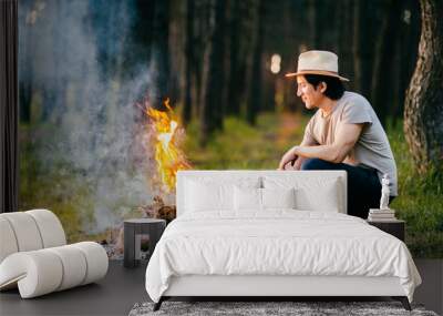 Native american indian peruvian indigenous man in straw hat sitting in forest outdoor in summer above bonfire with smoke and torch at hand. Shaman rite. Spiritual ceremony. Young sorcerer. Wall mural