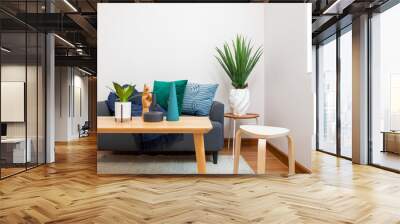 Modern living room with blue and green pillow on sofa. Coffee table with plant pot and ceramic vase. Wall mural