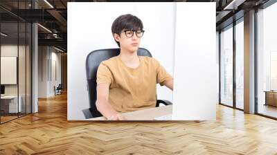 Serious teenage boy sitting on the chair while using computer at home. Online learning with his school classmates during lockdown. Wall mural