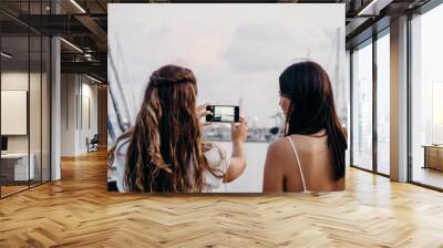 two women from behind take a photo with their mobile phone in the port Wall mural