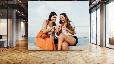 two women talk and you look at a mobile phone animatedly Wall mural