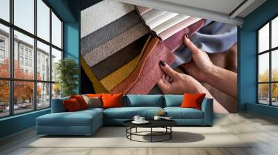 Choosing upholstery fabric color and texture from various colorful samples in a store. Female customer hands touching textile. Wall mural