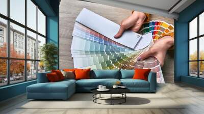 Color wheel for choosing paint tone. Hands of female interior designer working with palette for choosing colors. Creative process concept. Comparing options with matching hues. Wall mural