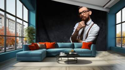 Young stylish hipster with cool hairstyle and beard dressed in white shirt and suspenders is thinking of a new creative idea looking at viewer Wall mural