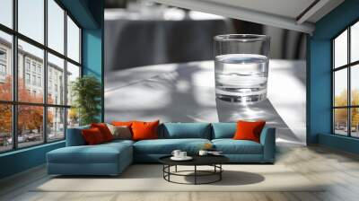 Glass of pure water with light reflection and shadow on white table of restaurant.  Wall mural