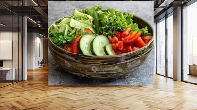 High angle of ceramic bowl with tasty healthy salad and vegetables placed with sliced cucumber and tomato with cutlery and fabric over gray table. Wall mural