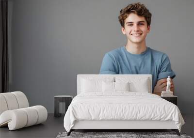 Indoor portrait of young european caucasian man isolated on gray background, standing in blue t-shirt with crossed arms, smiling and looking straight at camera.  Wall mural