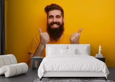 Young handsome man with beard over isolated yellow background with thumbs up because something good has happened. Wall mural